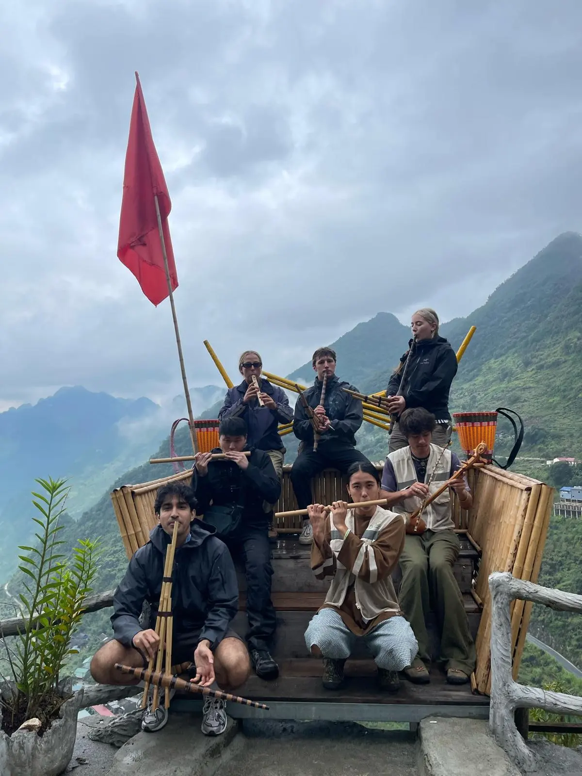 The group sitting on a bamboo platform above the valley, playing local pipes